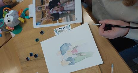 A person painting a family photo using watercolours.