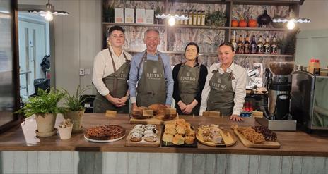 Staff from Bistro at the Courthouse stand behind the restaurants counter, with plenty of bakes and sweet treats in front of them