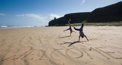 Image of beach with cliffs and sea in the background. The iconic Mussenden Temple is visible in the distance. In the foreground, 'welcome' has been ca