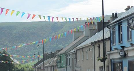 Cushendall street with various coloured flags strung between lamp-posts.