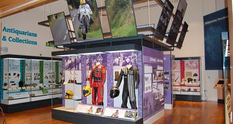 A glazed exhibition space showing racing gear worn by the face road motorbike racer Joey Dunlop