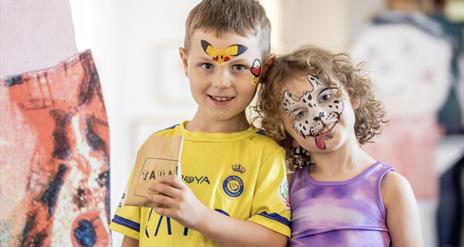 Two children with painted faces smile at the camera.