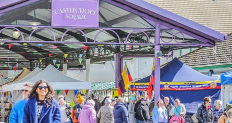 people walking through a market square with stalls