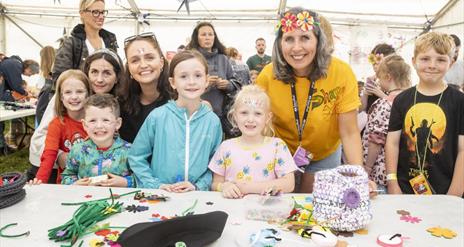 Children and adults  smiling in front of a table of colourful crafts and expressive pendants.