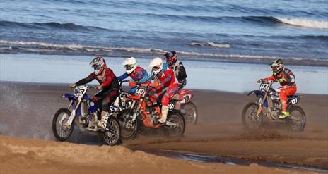 Riders on the sand with waves in the background