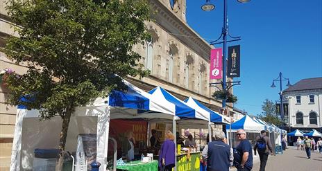 people browsing outdoor market stall tents on a sunny day