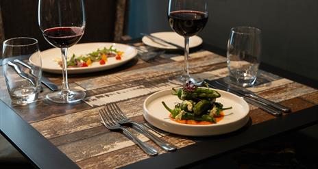 dishes of food and red wine sit on a wooden dining table