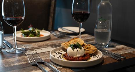 dishes of food and wine glasses sit on top of a wooden table