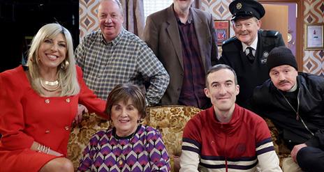 Image shows a family of seven people sitting on a sofa