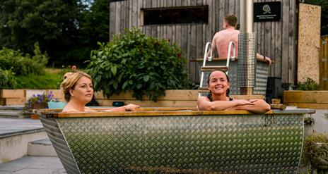 Two ladies relax in an outdoor shared tub