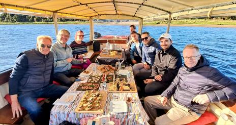 a group onboard ariver boat with various trays of food sat on the table infront of them