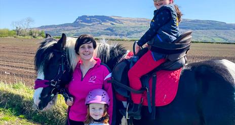 a woman and two children pose with a horse with Binevenagh Mountain in the background