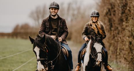 a man and woman on horseback on a countryside trail