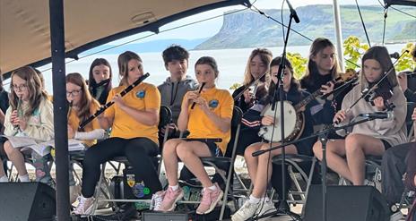 A row of children all play traditional instruments by the sea front at Ballycastle.