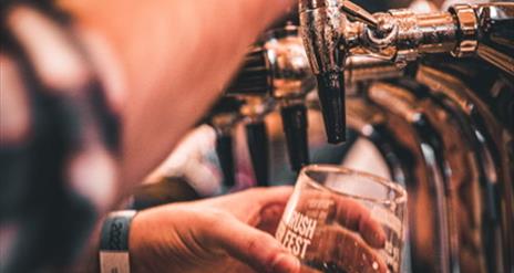 Image shows a man pouring a pint of beer in a 'Portrush Beer Fest' branded glass