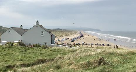A view over Portstewart Strand in the busy summer season with cars parked all along the beach and families enjoying their day out.
