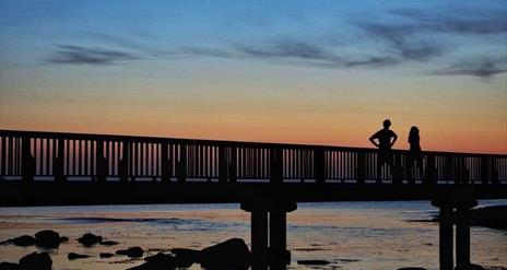 Couple standing on wooden pier looking at the sunset  at Ballycastle Beach.