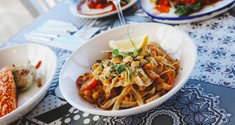 a bowl of taglatelle pasta sits on a mosaic style table surrounded by other plates of food