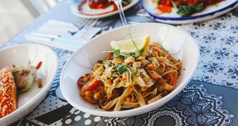 a bowl of taglatelle pasta sits on a mosaic style table surrounded by other plates of food