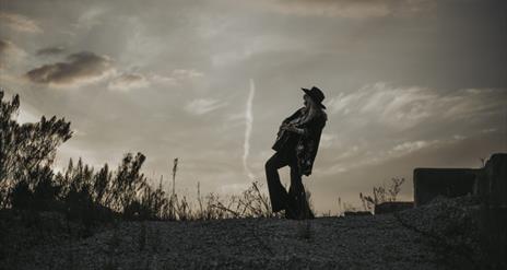 black and white image of kimmi rhodes playing a guitar silhoutted against the sky,