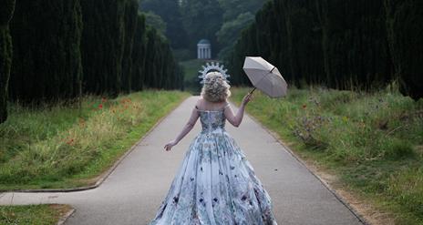 Woman in a ballgown walking through an ornate park.