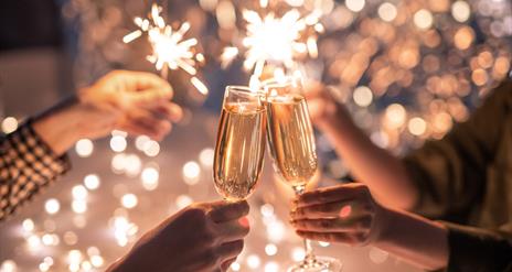 Wine glasses clink together in front of sparklers on New Year's Eve