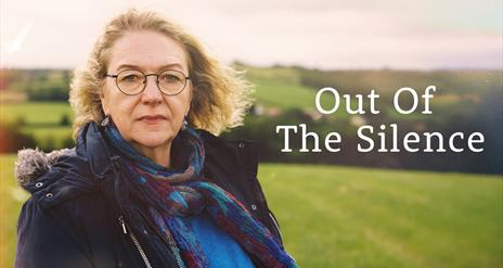 A woman with blond hair and round spectacles stands in a field looking towards the camera. Beside her the title "Out of the Silence" is written in whi