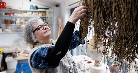 Patricia reaches for dried grass in her workshop