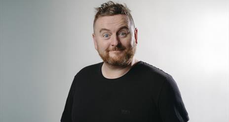 Paddy McDonnell smiles for the camera against a grey background with bright light.