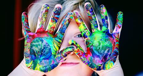 a child peaks through hands that are covered in paint