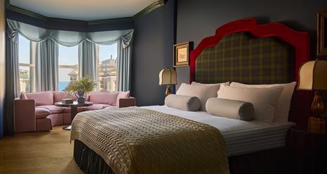 interior of double bedroom at Adelphi Hotel - features a tartan headboard and knitted throw on the bed, as well as a low pink sofa by the window overl