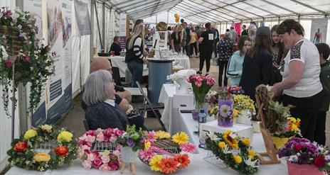 Crowds in a marquee looking at floral arrangements on a table covered with a white tablecloth