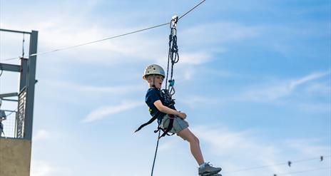 A boy in a blue outfit and white helmet harnessed to a zipline