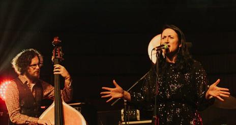 Image of Ann Nola sinting on stage into a microphone and rohan armstrong to her right plucking a double bass.