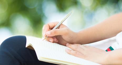 Close up of a person sitting outdoors writing in a note book.