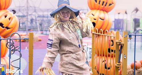 a person dressed as a scarecrow poses at Blair's Holiday Park, surrounded by pumpkin decorations