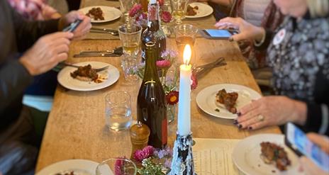 people are eating at a large wooden table by candlelight