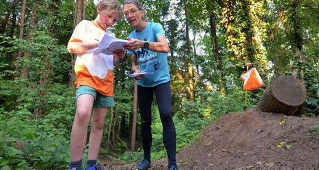 A woman and a young boy in the woods, reading a map together.