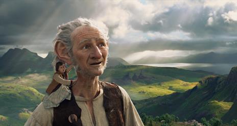 The BFG stands with a small child on his shoulder, with the countryside in the background.