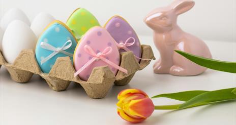 a porcelain rabbit statue sits next to an egg box containing ceramic egg decorations