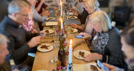 People sitting either side of a long wooden table decorated with candles and wine bottles.