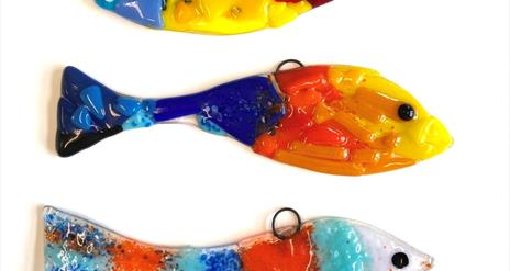Image shows three brightly coloured fish made from fused glass, one on top of the other