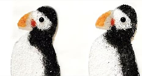 Two glass puffins facing left. They are flat against a white background.