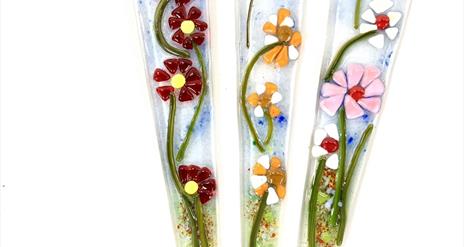 Image shows three glass stakes with flowers in bright colours