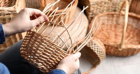 A basket being woven by hand. A collection of these baskets is visible in the background.