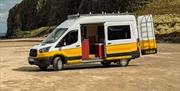 A white and yellow Karen & Co. campervan with its side door open on Downhill beach, below the cliffs