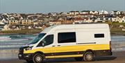 A white and yellow Karen & Co. campervan on a beach on the north coast, with the town behind