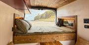 The bed inside a Karen & Co. campervan, with the back doors open onto a beach and cliffs