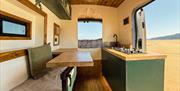 Inside a Karen & Co. campervan: a fitted kitchen with a hob and sink, and a table with a bench seat