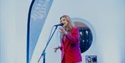 a woman sings in to a microphone on stage with a branded Atlantic Sessions flag beside her